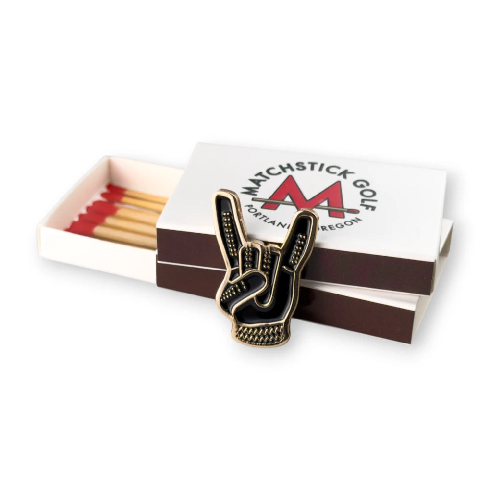 black and gold  devil horns golf ball marker leaning on matchbox packaging