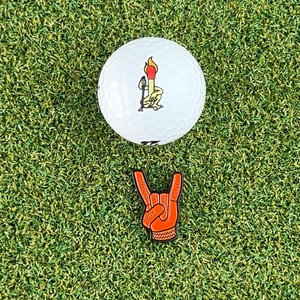 orange devil horns golf ball marker on grass next to white golf ball