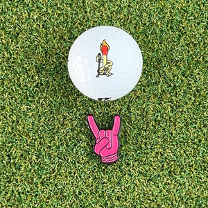 pink devil horns golf ball marker on grass next to white golf ball