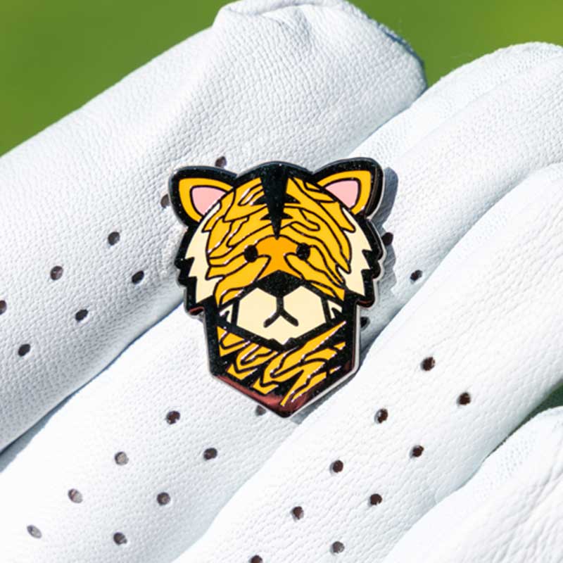 wood tiger golf ball marker held in fingers of golf glove laid flat