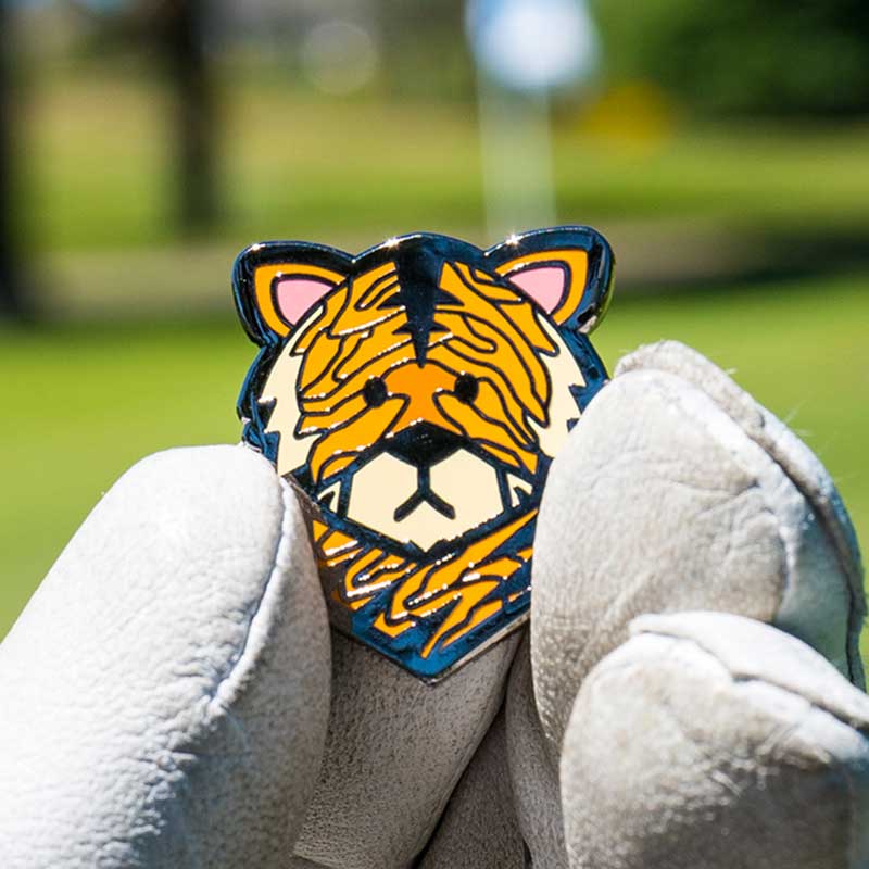 wood tiger golf ball marker held in golf glove fingers on green